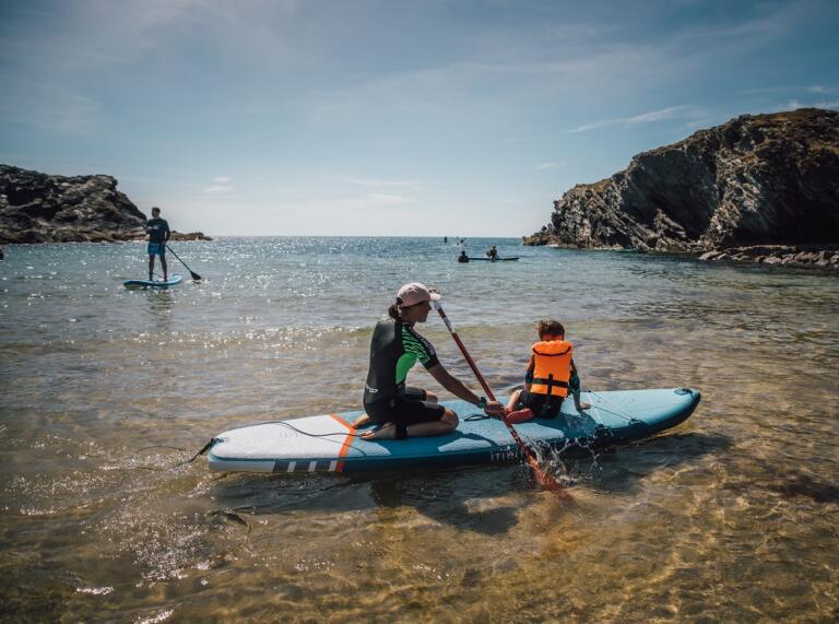 Two adults and a child on paddleboards in shallow, sparkly coastal waters 