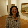 A profile image of a woman with brown hair and wearing a black and white shirt.