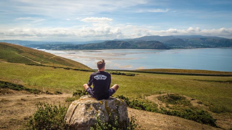 Homme assis sur un rocher regardant l'estuaire dans le nord du Pays de Galles.