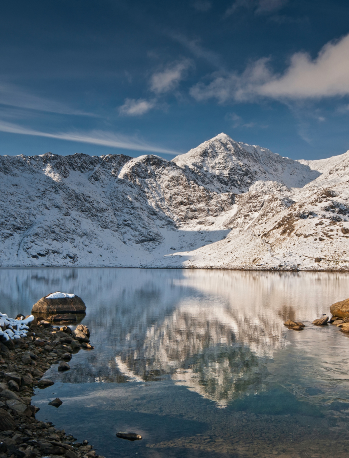 Walker looking towards snow-covered summit of Yr Wyddfa (Snowdon)from Llyn Llydaw lake, Snowdonia