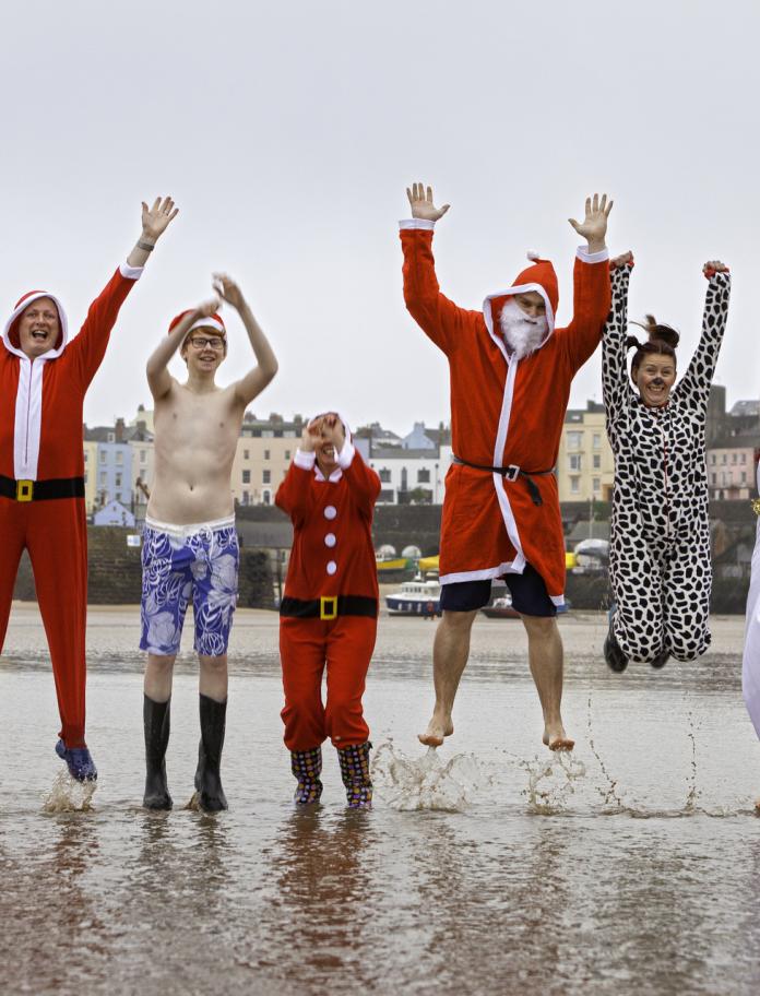 Des personnes en costumes de Noël sautent en l'air dans la mer.