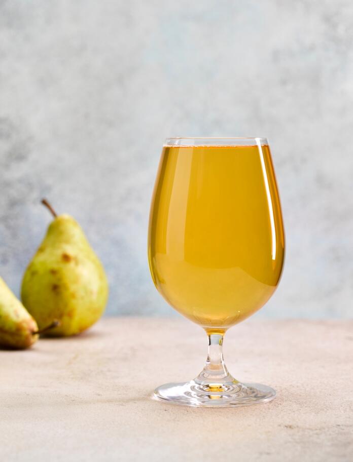 A glass of pear cider next to some pears.