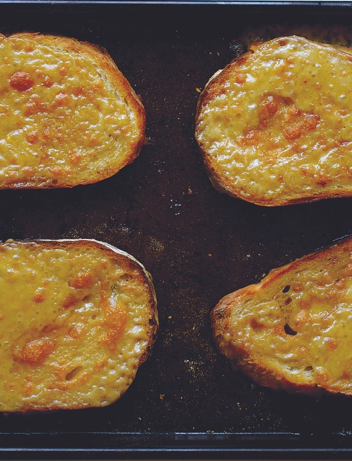 Drei Scheiben Welsh Rarebit auf einem schwarzen Tablett.