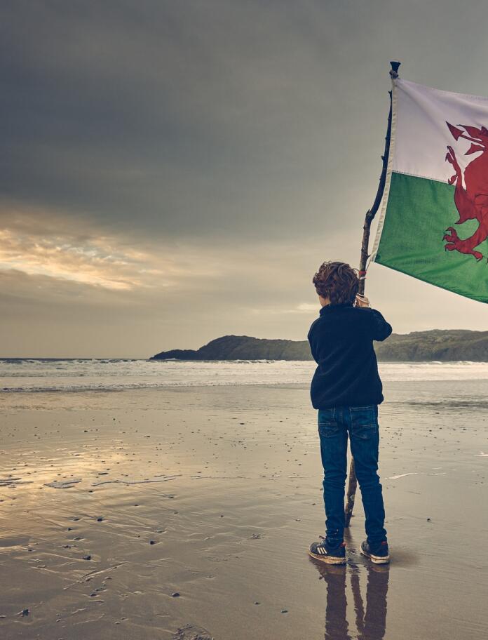 A child waving the Welsh flag on a beach.