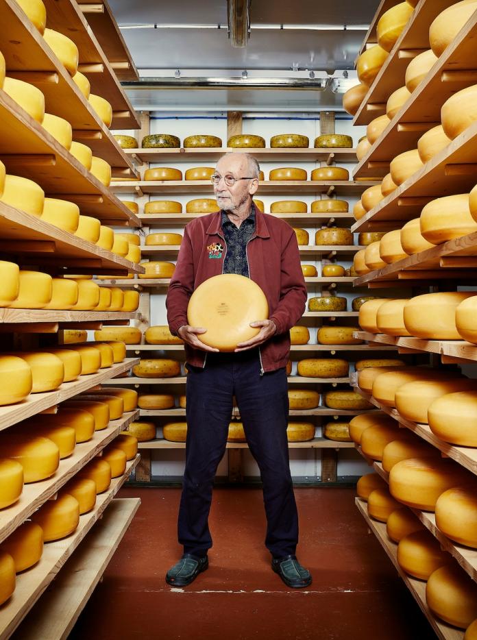 Ein Mann steht in einem Lagerraum, umgeben von Regalen mit Käse