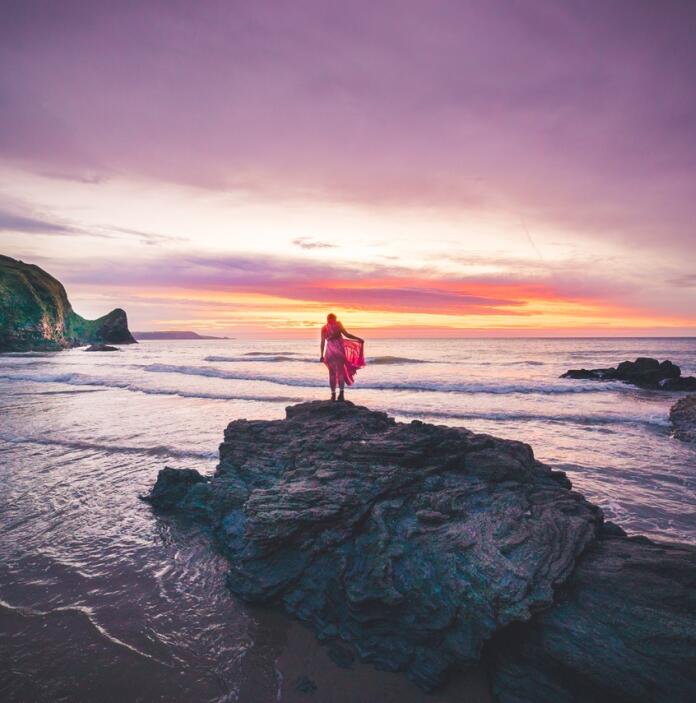 Une personne debout sur un rocher devant un incroyable coucher de soleil violet.