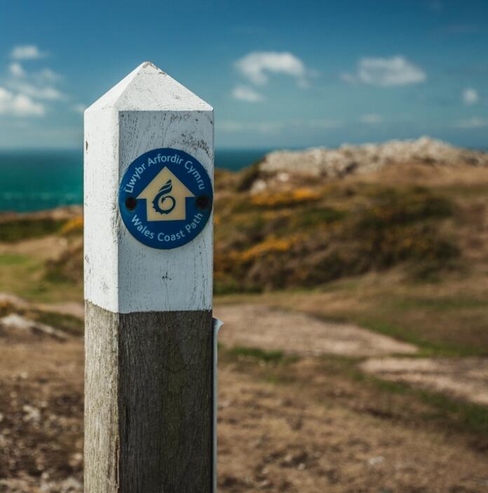 Un cartel de madera con una insignia de la Ruta de la costa de Gales, contra un fondo de un mar azul y una costa