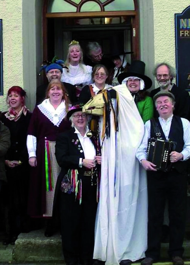 Un grupo de personas afuera de una casa pública con la Mari Lwyd al frente