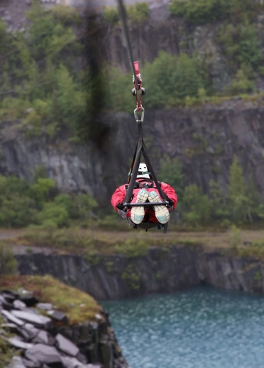 Une personne dans un harnais descend une tyrolienne sur fond de montagne.