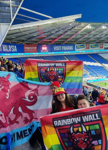 Un grupo de aficionados al fútbol galés sosteniendo pancartas arcoíris en un estadio de fútbol