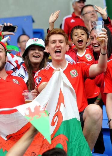Un grupo de personas con camisetas de fútbol de Gales sonriendo y sosteniendo la bandera galesa.