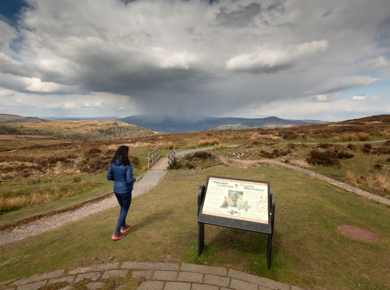 A woman walking down a path surrounded by green landscape.