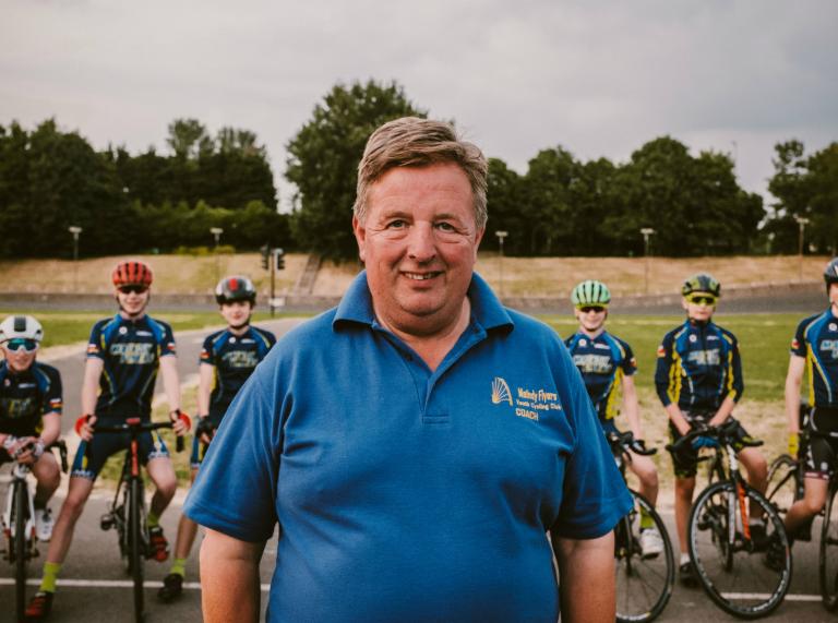 El entrenador de ciclismo Alan Davies MBE en primer plano con miembros del club de ciclismo juvenil Maindy Flyers de pie con bicicletas detrás