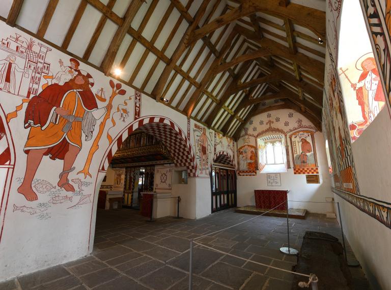 L’intérieur d’une église avec des arcades, des peintures murales sur les murs et du bois au plafond.