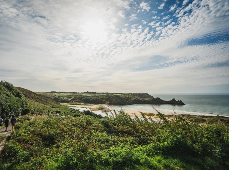 Scène côtière ensoleillée et pittoresque avec une baie de sable entourée de falaises verdoyantes.