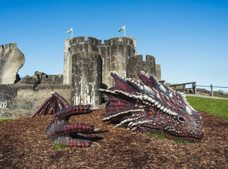 Una gran escultura de un dragón rojo frente a un gran castillo antiguo.