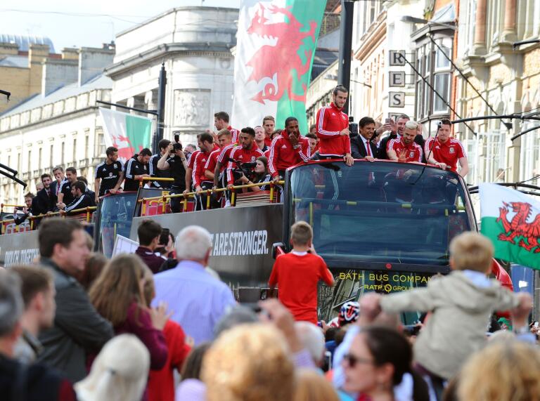 El equipo de fútbol de Gales en la parte superior de su autobús turístico saludando a las multitudes abajo.