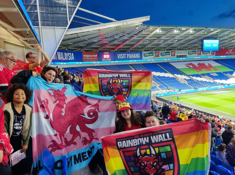 Un groupe de fans de football gallois tenant des bannières arc-en-ciel dans un stade de football