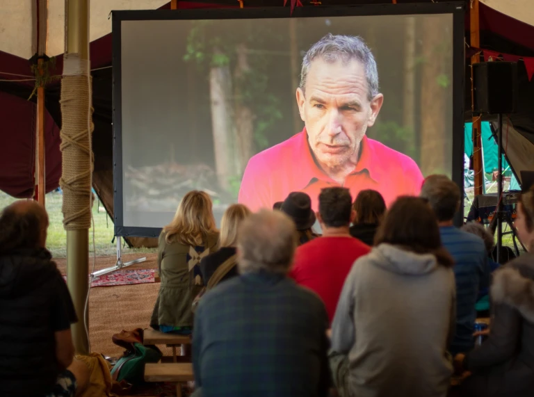 Eine Gruppe von Menschen sitzt und schaut einen Film auf einer Projektionsleinwand.