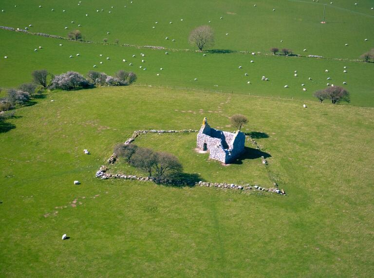 vista aérea de la antigua capilla rodeada de un campo con ovejas.