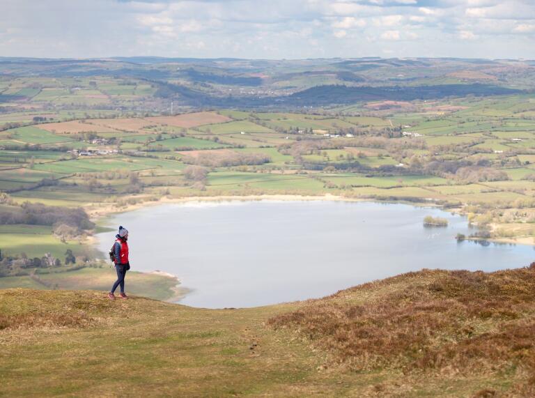 A person walking over the hills with a large lake in the background.