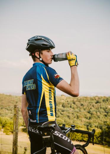 Un ciclista está sentado en su bicicleta, descansando y bebiendo de una botella de agua