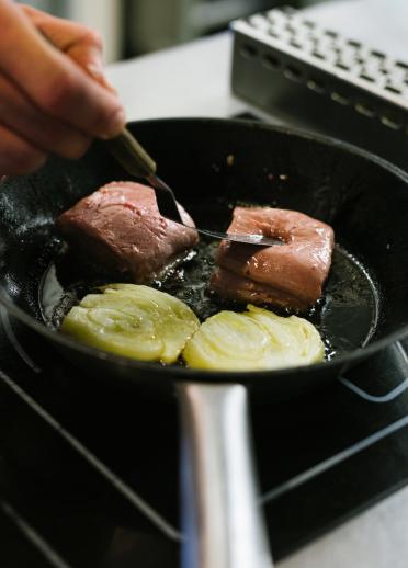La mano de un chef cocina carne en una sartén sobre una estufa en una cocina.