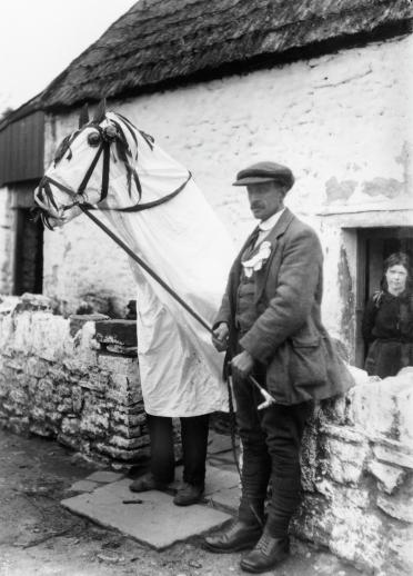 A Mari Lwyd and a man outside a cottage.