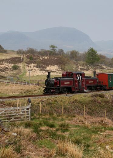 Una máquina de vapor roja y verde moviéndose a lo largo de una vía frente a un fondo montañoso