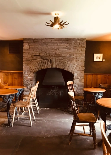El interior del restaurante con mesa y sillas de madera y una gran chimenea al fondo.