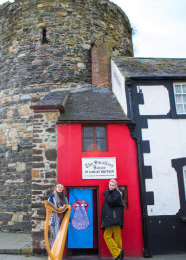 2 musicians, one with harp, outside the Smallest House in Great Britain.