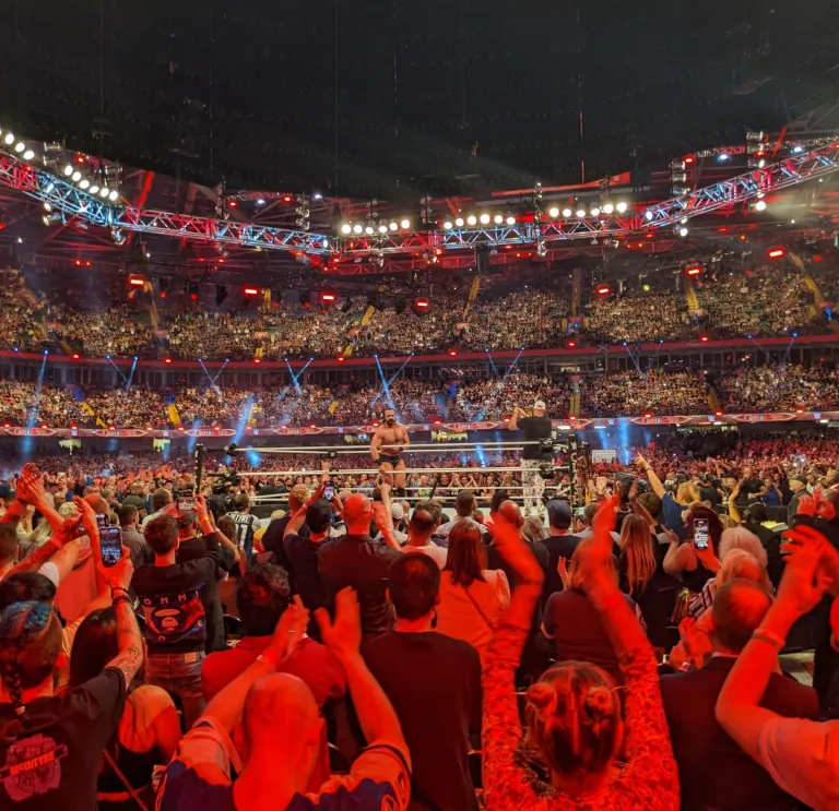 A wrestler standing in a wrestling ring in the middle of a huge stadium, surrounded by cheering fans.