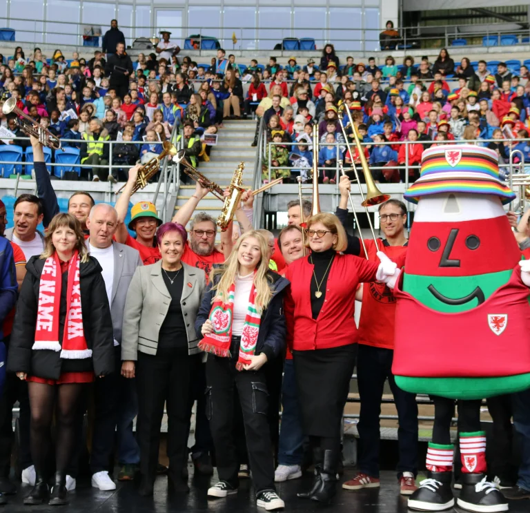 A group of people and mascots wearing Wales kit cheering