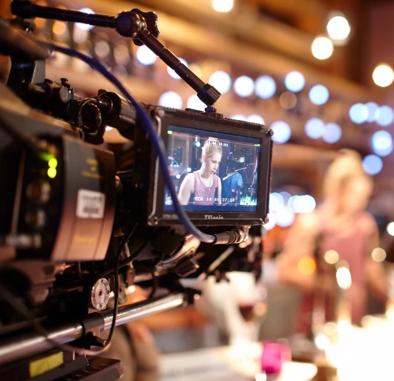 A professional camera in a studio where filming is taking place, with an actor showing through the viewfinder