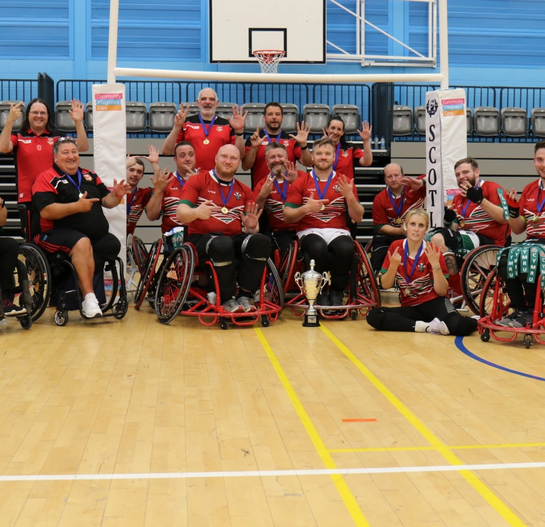 A team of wheelchair rugby players with a silver cup. 