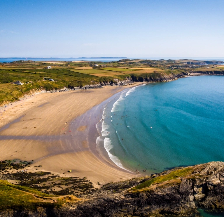 A wide sandy cove with blue seas and cliffs.