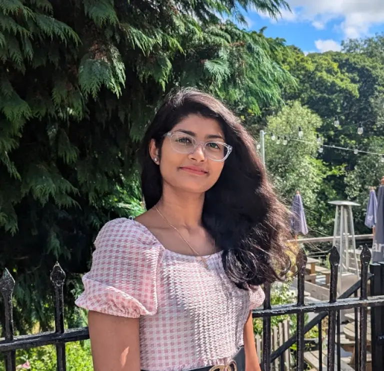 A young girl stood in pink dress smiling in front of forest