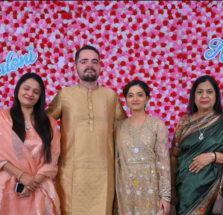 6 people stood in front of pink and red background smiling in Indian clothing