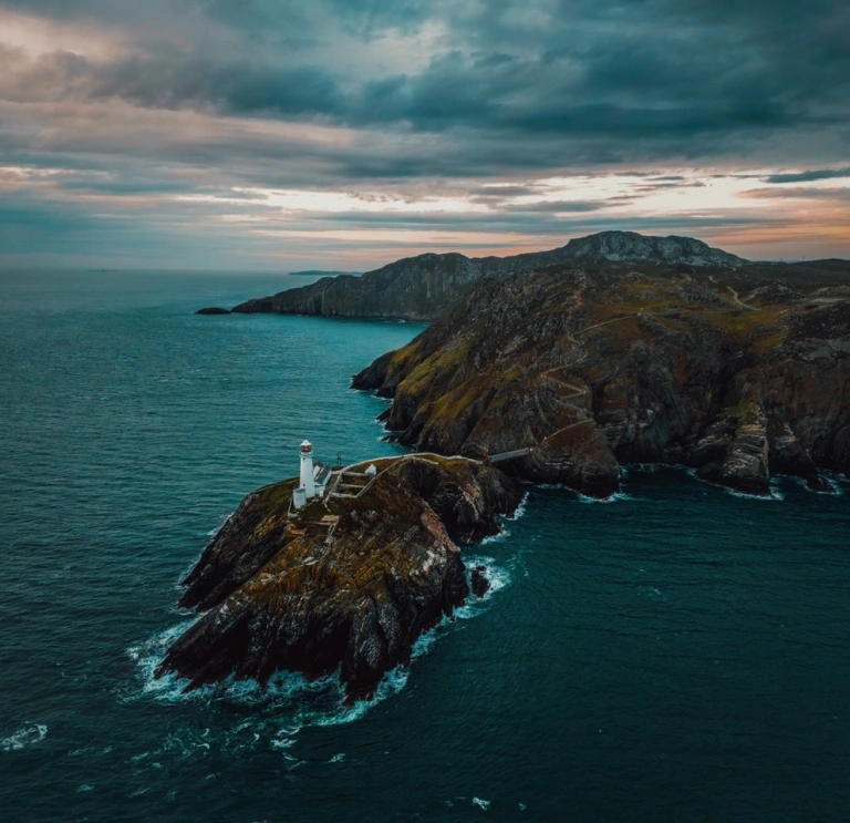 Dramatic coastal shot showing a lighthouse on exposed outlying rocky land, with blue seas and waves all around 