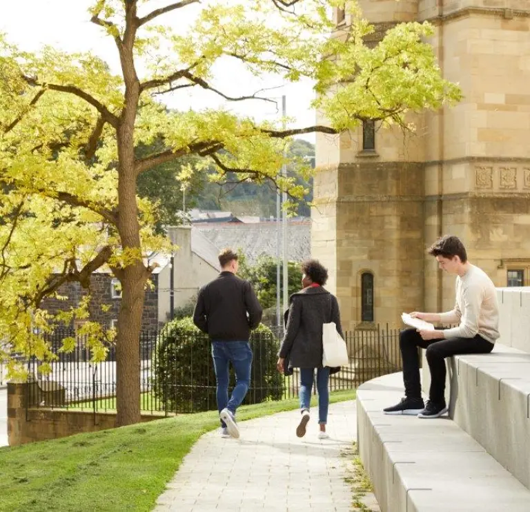 Two people walking and one sat on steps Bangor University