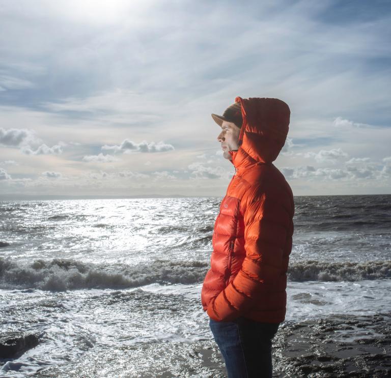 Ein Mann in einer warmen orangefarbenen Jacke, der auf das Meer schaut