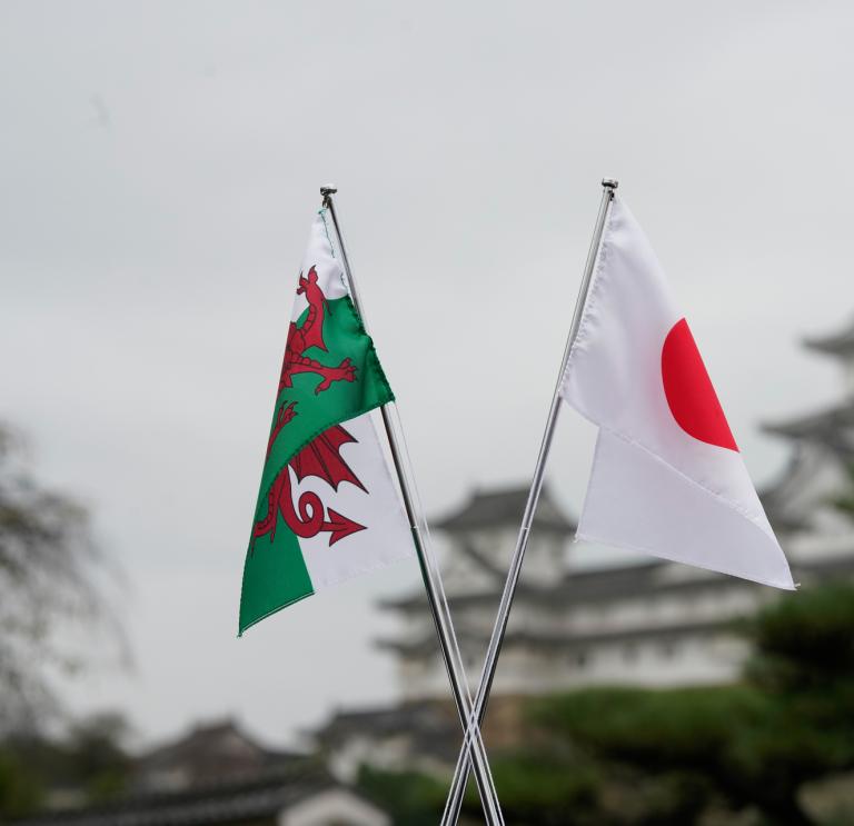 una bandera de Gales y una bandera japonesa frente al castillo de Himeji