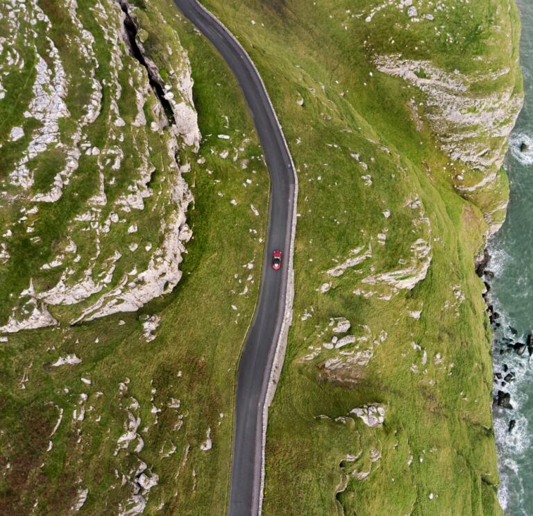 Vue aérienne d'une voiture sur une route côtière montagneuse.