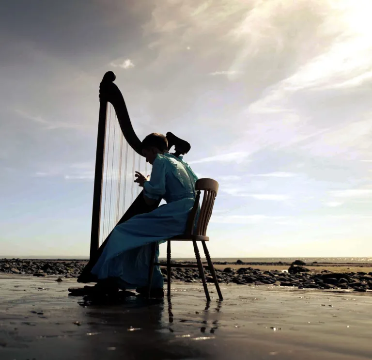 Une jeune harpiste en robe longue, assise et jouant de la harpe sur une belle plage déserte.