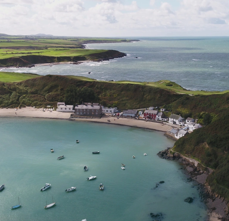 View of a wide bay from above with green hills and blue sea on which boats are morred