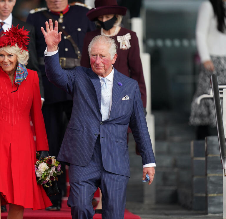 El rey Carlos III acompañado por la reina consorte, bajando unas escaleras y saludando a la multitud