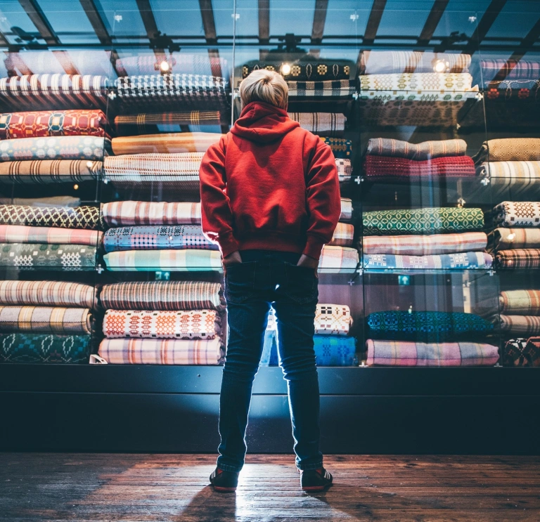 Un jeune garçon regarde une armoire colorée remplie de couvertures galloises.