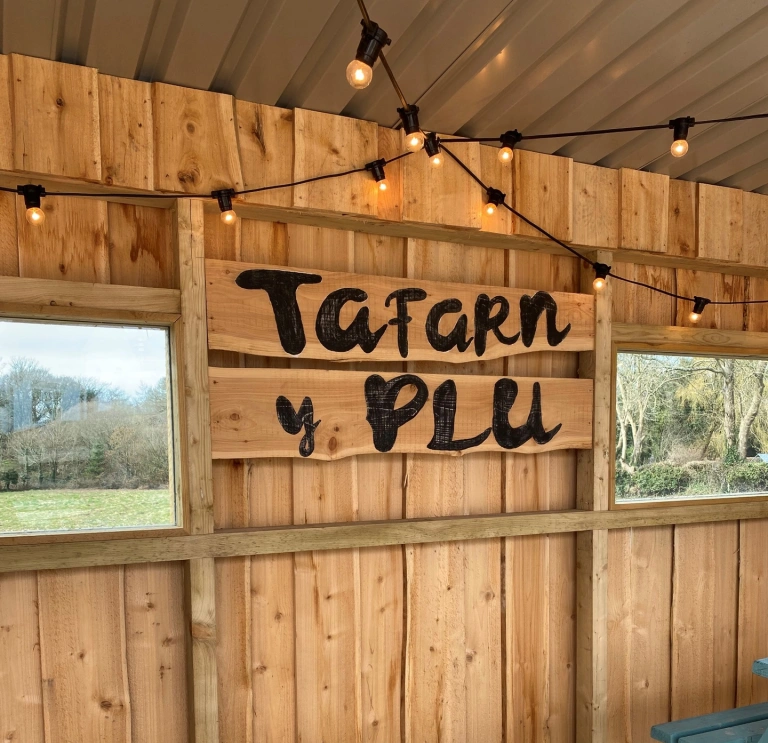 Inside a wooden garden shelter with 'Tafarn y Plu' written on a sign.