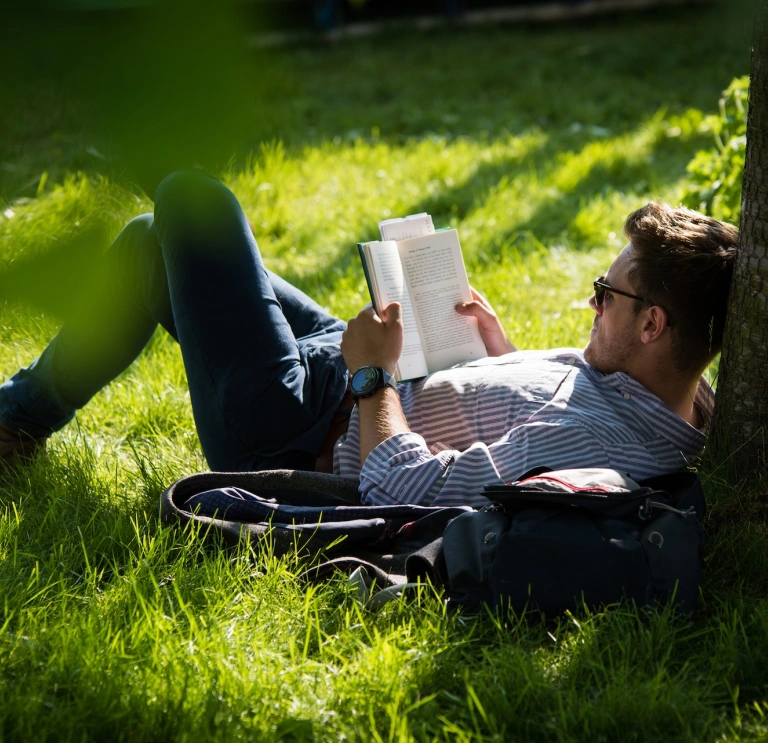 Eine Person, die auf dem Gras liegt und ein Buch liest