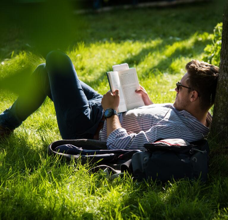 Une personne allongée sur l'herbe en train de lire un livre.